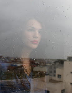 woman's face reflected on clear glass window with water droplets thumbnail
