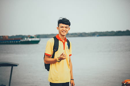 man wearing yellow and orange polo shirt standing near body of water at daytime thumbnail