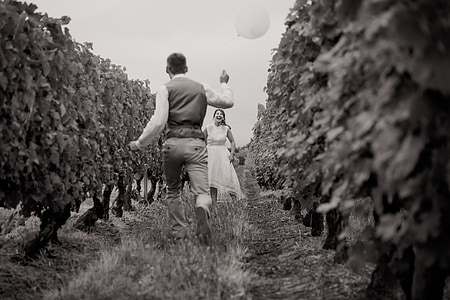 grayscale photography of groom holding balloon while running towards his bride thumbnail