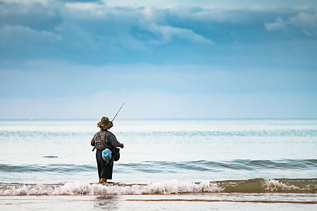 person standing on seashore holding fishing rod thumbnail