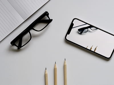flatlay photo of black eyeglasses and black smartphone with three pencils thumbnail
