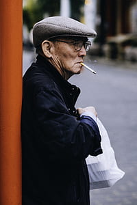 man smoking cigarette while leaning on orange pole thumbnail
