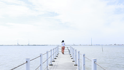 woman standing on dock looking at sea under cloudy sky during daytime thumbnail