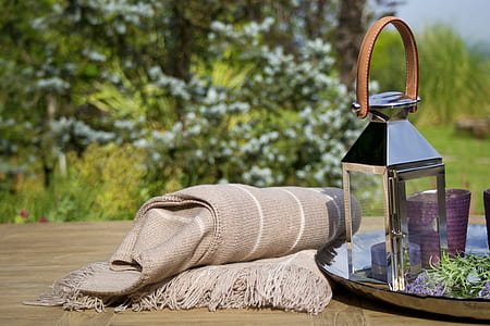 gray blanket with fringe beside gray stainless steel framed candle lantern on gray tray at daytime thumbnail