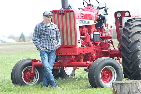 man standing beside red tractor outdoors thumbnail