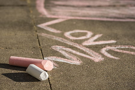 two pink and white chalks on asphalt road with love graffiti during daytime thumbnail