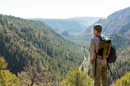 man with backpack looking at tree covered mountain thumbnail