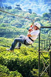 smiling man ziplining above green tree canopy during daytime thumbnail