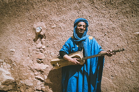 Man Wearing Blue Top Holding Brown String Instrument thumbnail