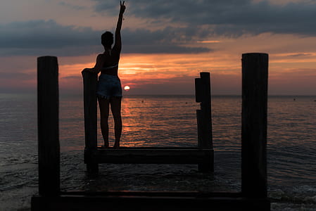 silhouette of woman standing on water dock during golden hour thumbnail