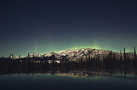 landscape photography of lake across mountain covered with snow with trees under stars thumbnail