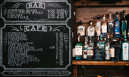assorted alcoholic bottles on brown wooden rack beside black chalkboard thumbnail