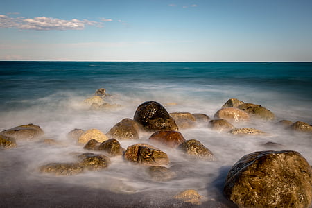 brown rocks near body of water under white and blue sky thumbnail