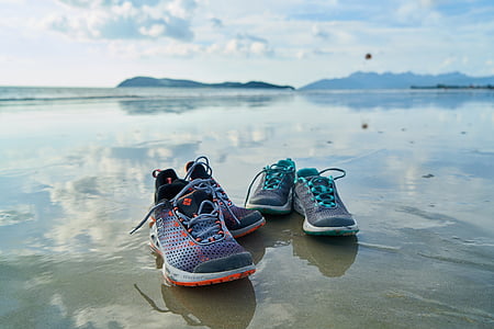 two pairs of athletic shoes on grey sand beach shore thumbnail