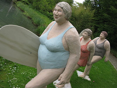 woman carrying surfboard statue near body of water thumbnail