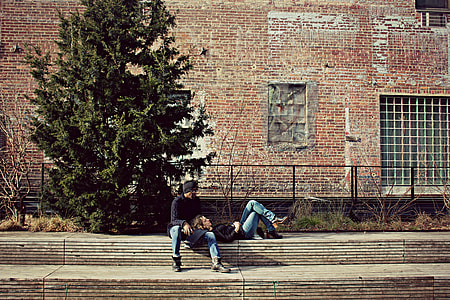 man and woman in blue denim pants seating on concrete gather thumbnail