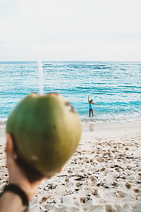 person holding coconut while facing body of water thumbnail