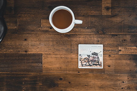 White Ceramic Mug With Coffee Beside Photo of Two Mountain Bikes thumbnail