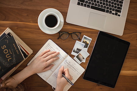 flay lay photography of woman writing on pen beside coffee cup and MacBook Pro thumbnail