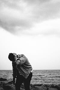 grayscale photo of man standing near seashore thumbnail