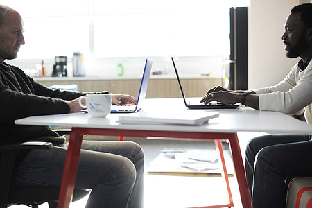 two men sitting in front of white table while using laptops thumbnail