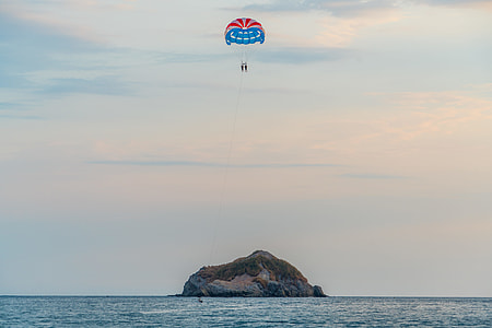 person with parachute above island during daytime thumbnail