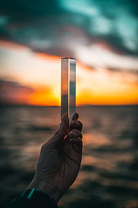 person holding clear glass against the horizon during sunset thumbnail