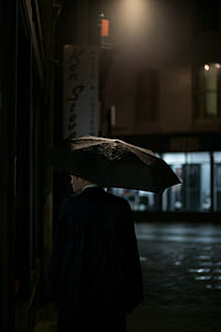 man holding black umbrella while walking on street during night thumbnail