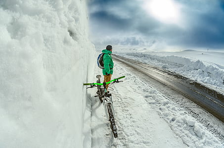 man in green coat standing beside ice wall with green bicycle during daytime thumbnail