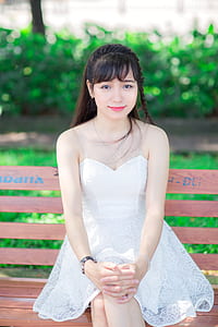 woman wearing white spaghetti strap lace dress sitting on bench chair near plant at daytime thumbnail