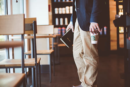 person holding book and cup standing near chair thumbnail