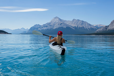 woman kayaking in calm body of water with mountain alps in distance during daytime thumbnail