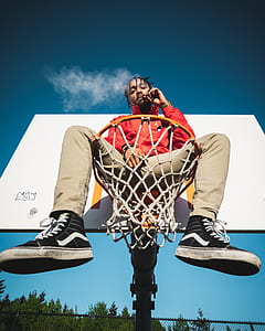 man wearing yellow zip-up jacket sitting on orange basketball hoop thumbnail