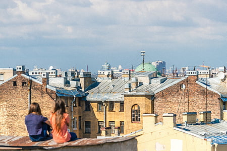 two woman sitting on roof in front of buildings during daytime thumbnail