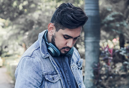man wearing blue denim jacket looking downward near tree at daytime thumbnail