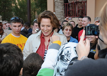 smiling woman surrounded with people facing her and taking photo of her thumbnail