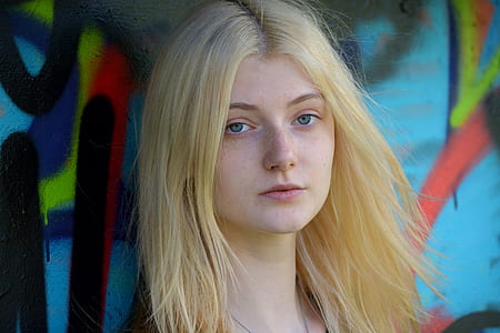 woman in blonde hair leaning on blue wall thumbnail