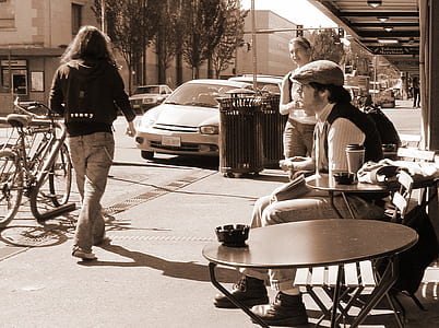 Man in Black and White Long-sleeved Shirt Sits on Brown Wooden Chair Facing Road thumbnail