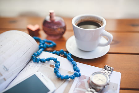 beaded blue necklace on book between white cup with coffee and analog watch thumbnail