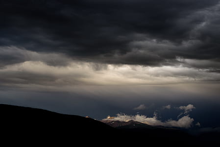 silhouette photography of mountain under nimbus clouds thumbnail