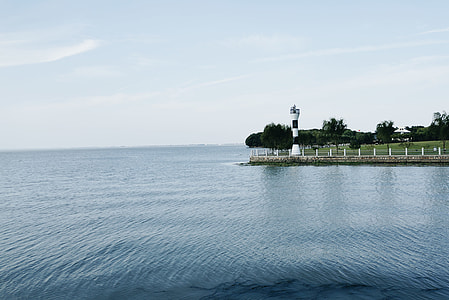 body of water near green island and lighthouse at daytime thumbnail