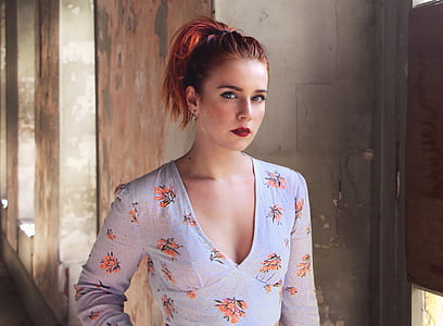 woman wearing blue and orange floral long-sleeved top standing gray concrete wall thumbnail