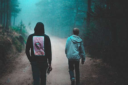 two men walking on road surrounded by trees thumbnail