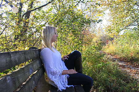 woman in white dress sits on bench chair near  tall trees at daytime thumbnail