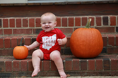 baby sitting beside two pumpkins while smiling thumbnail