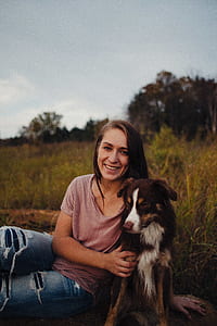 woman in beige scoop-neck shirt sitting beside medium short-coated black and white dog thumbnail