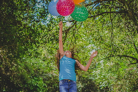 girl holding multicolored balloon near tree thumbnail