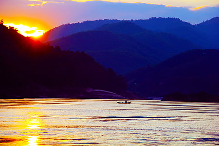 person riding on boat at body of water with mountains as background thumbnail