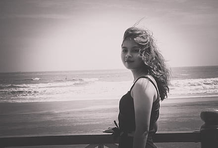 Grayscale Photo of Woman Wearing Tank Top Standing Near Seashore thumbnail