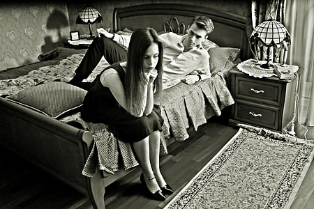 grayscale photo of woman sitting on bed near man lying on bed thumbnail